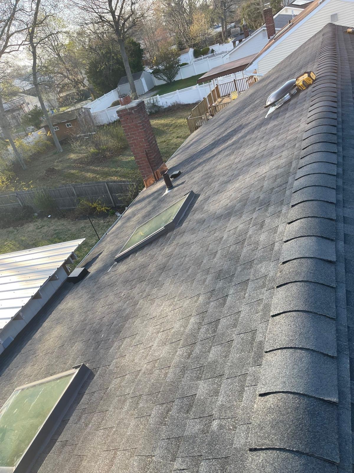Completed shingle roof with skylights, chimney flashing and ridge vent installed by EZ Roofing and Builders on Long Island