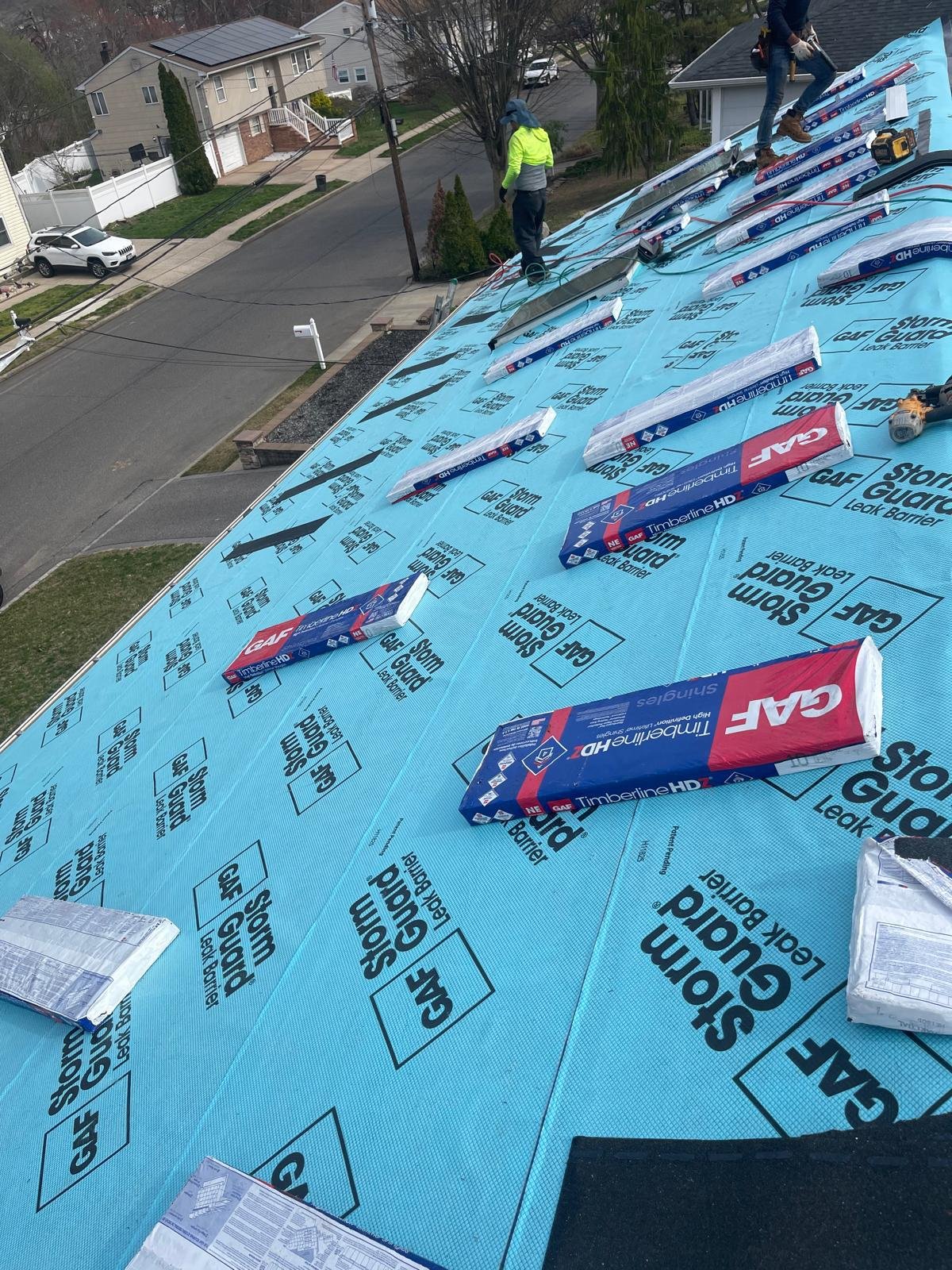 EZ Roofing and Builders installers staging GAF Timberline HDZ shingle bundles on a Nassau County roof